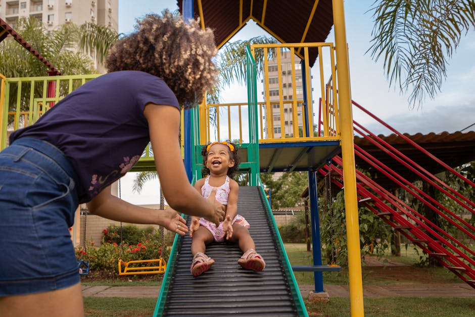 A young girl with afro hair joyfully slides down, playing in a vibrant outdoor playground.