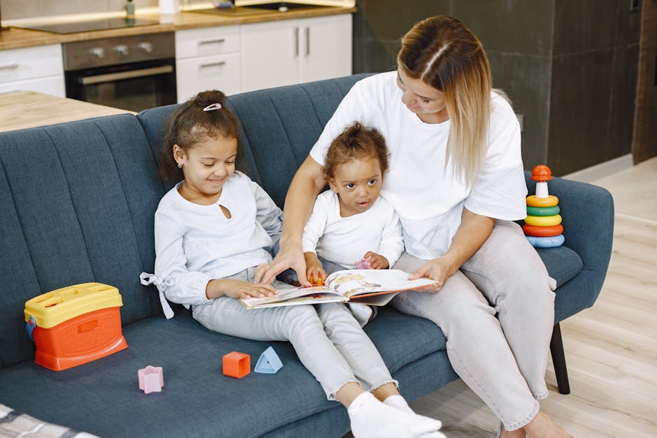 Mother reading a storybook to her two daughters on a blue sofa with toys around.